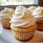 Close-up of several moist vanilla cupcakes topped with thick swirls of white buttercream frosting.