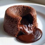 Close-up of a warm chocolate lava cake with molten center oozing onto a white plate.