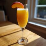 A fizzy, orange-colored bellini recipe cocktail garnished with a fresh peach slice in a champagne flute.