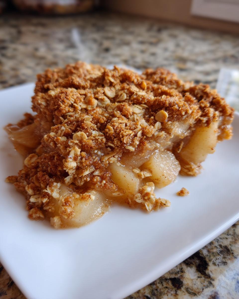 A close-up shot of a serving of warm pear crisp with a thick, crumbly oat topping on a white plate.