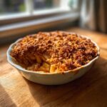A freshly baked apple crisp with a golden, crunchy oat topping served in a white baking dish.
