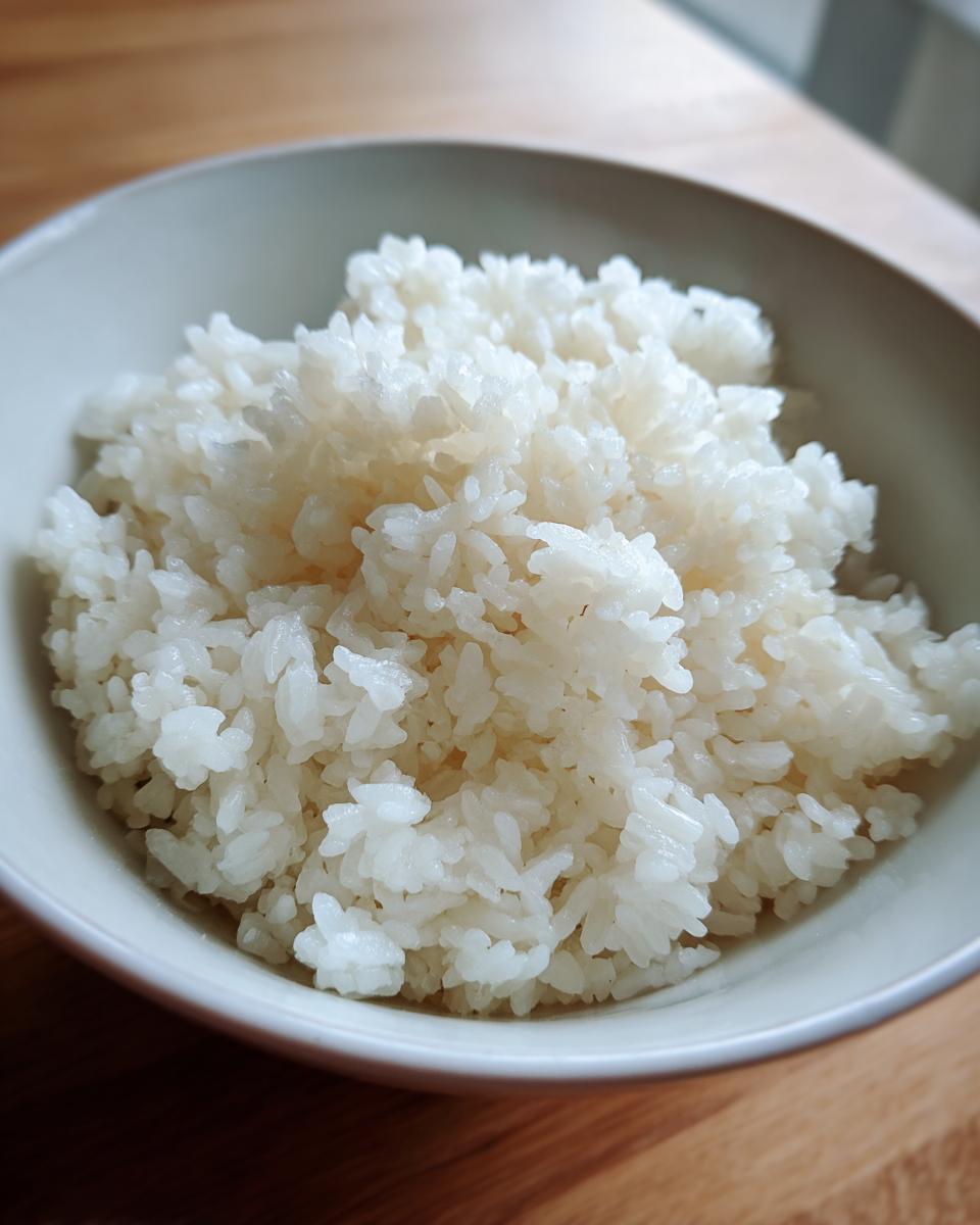 Close-up of perfectly cooked, slightly glossy sushi rice grains mounded in a light-colored bowl.