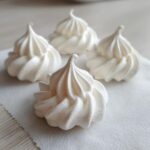 Four perfectly piped, bright white meringue cookies resting on a white napkin.