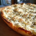 Close-up of a freshly baked pizza topped generously with creamy white pizza sauce and dried herbs.