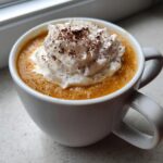 Close-up of a rich pumpkin spice latte topped with a generous swirl of whipped cream and a dusting of spice.