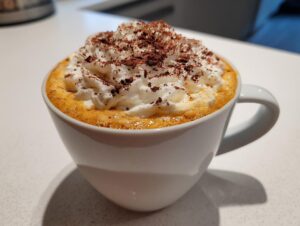 Close-up of a creamy pumpkin spice latte topped with a mountain of whipped cream and dusted with cocoa powder.