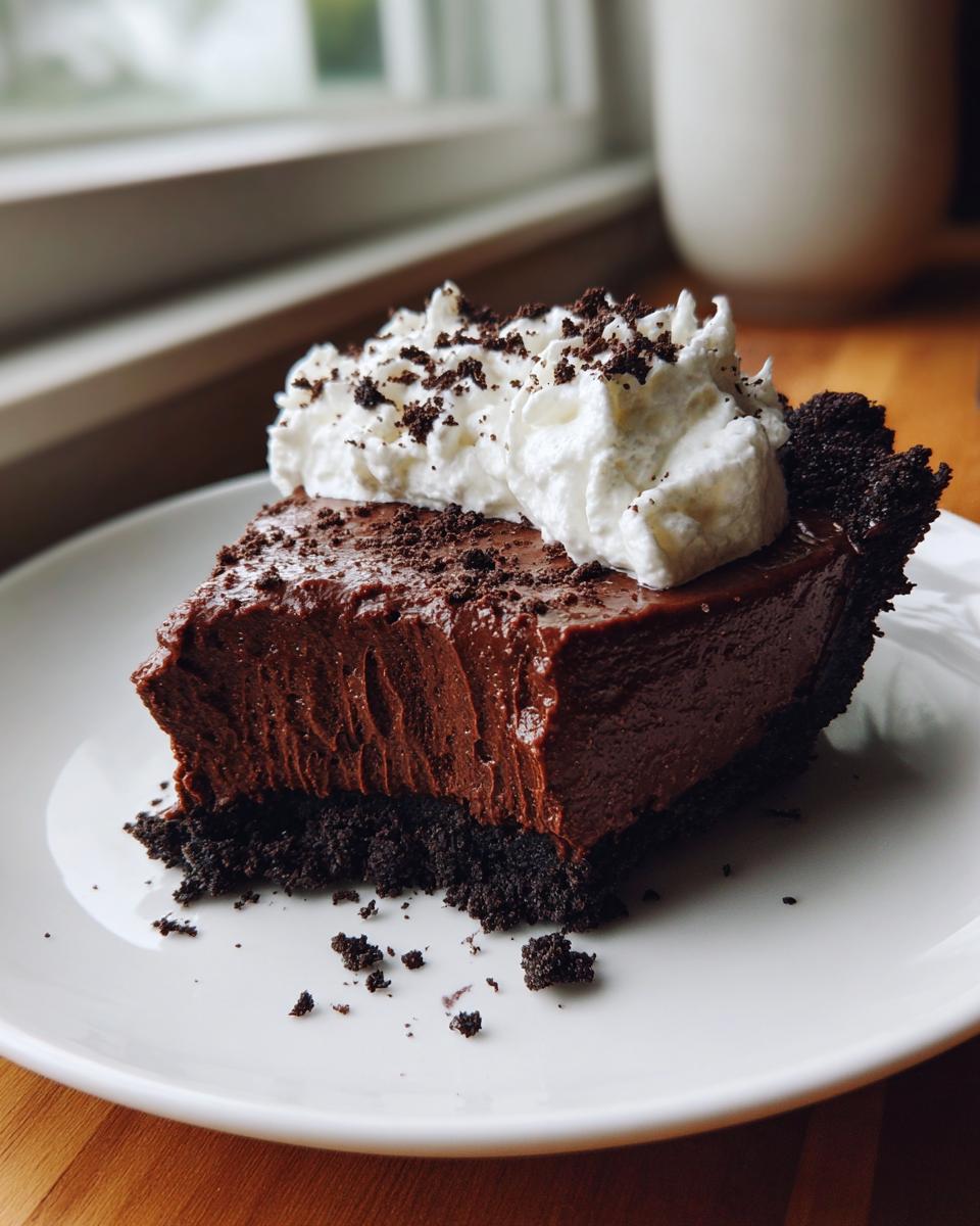 A decadent slice of chocolate mousse pie with a dark crust, topped with whipped cream and chocolate crumbs.