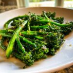 Close-up of vibrant green, roasted broccolini tossed in oil and seasonings served on a white plate.