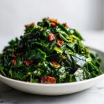 A close-up of a bowl filled with tender, dark green collard greens topped with crispy bacon bits.