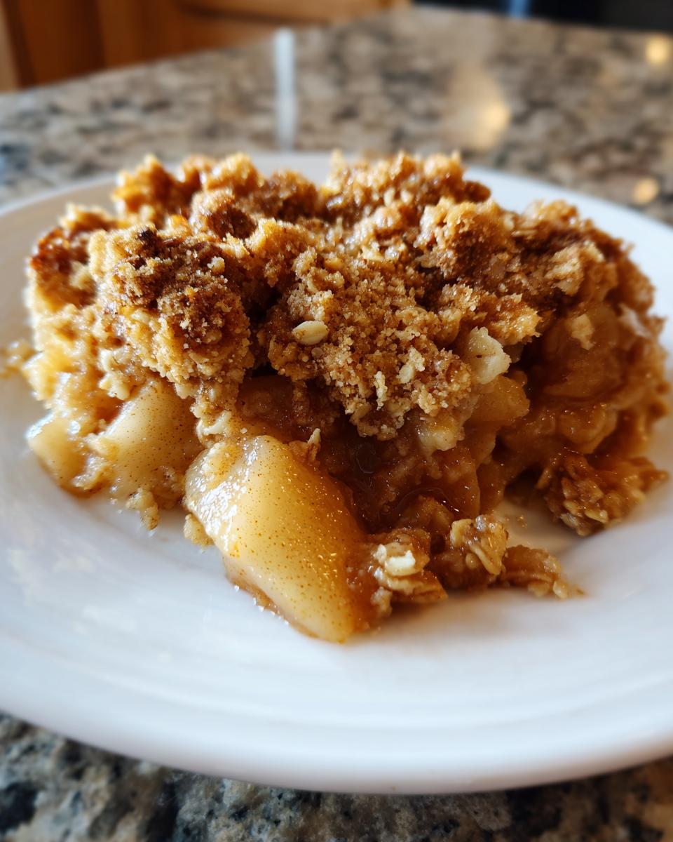 Close-up of a warm serving of pear crisp with a thick, crunchy oat topping on a white plate.
