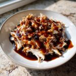 Close-up of shredded crockpot teriyaki chicken generously drizzled with thick, glossy teriyaki sauce in a light bowl.