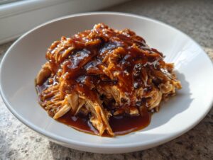 A close-up of shredded crockpot teriyaki chicken smothered in glossy teriyaki sauce served in a white bowl.
