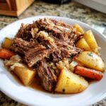 A bowl filled with tender shredded pork and sauerkraut, served alongside chunks of roasted potatoes and carrots.