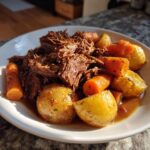 A white bowl filled with shredded pot roast, tender carrots, and golden potatoes sitting in rich gravy.