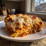 A generous, layered slice of skillet lasagna topped with bubbly, melted mozzarella cheese, served on a white plate.