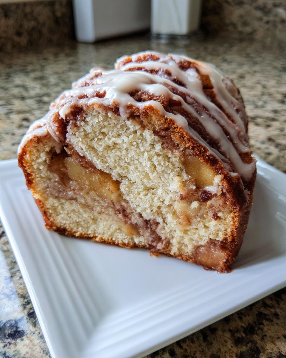 A thick slice of moist apple fritter bread showing chunks of apple filling and topped with a white vanilla glaze.