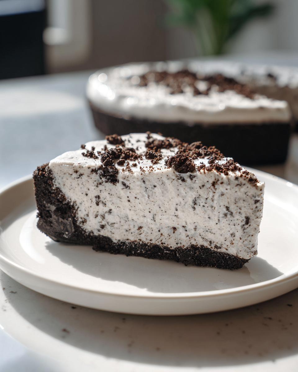 A generous slice of creamy Oreo pie with a dark chocolate crust, topped with cookie crumbs.
