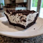 A close-up slice of creamy, no-bake Oreo pie with a dark chocolate crust and crushed topping.