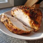 A slice cut from a perfectly cooked slow cooker turkey breast showing moist white meat and a seasoned, browned exterior.