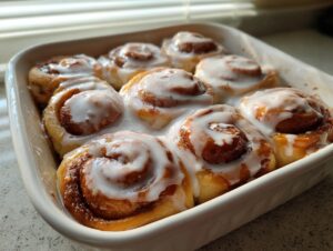 Close-up of freshly baked small batch cinnamon rolls topped with thick white icing in a white ceramic baking dish.
