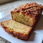 A loaf of snickerdoodle zucchini bread, partially sliced, showing green shreds of zucchini inside and a cinnamon sugar topping.