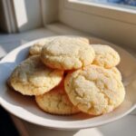 A stack of freshly baked soft sugar cookies generously coated in sparkling granulated sugar, resting on a white plate.
