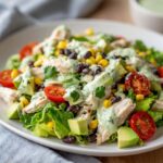 Close-up of a vibrant southwest chicken salad featuring sliced chicken, avocado, black beans, corn, tomatoes, and creamy cilantro dressing.