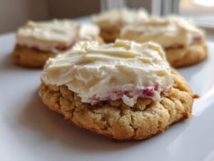 A close-up of one of the amazing strawberry cheesecake cookies topped with thick, creamy white frosting.