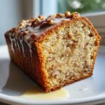 Close-up of a moist slice of sweet alabama pecan bread topped with pecan pieces and a white glaze.