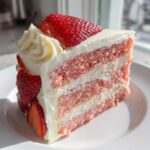 A decadent slice of two-layer strawberry cake featuring pink layers, white frosting, and fresh strawberry garnish.