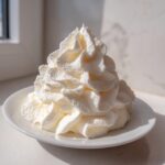 A large, perfectly piped swirl of creamy white vanilla buttercream frosting sitting on a small white plate.