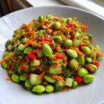 Close-up of a bright, colorful edamame salad featuring shelled edamame, shredded carrots, diced cucumber, and red pepper.