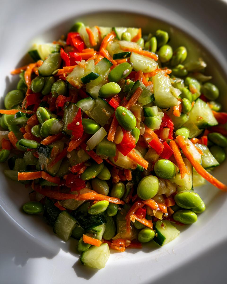 Close-up of a vibrant edamame salad featuring bright green edamame, shredded carrots, diced cucumber, and red pepper.