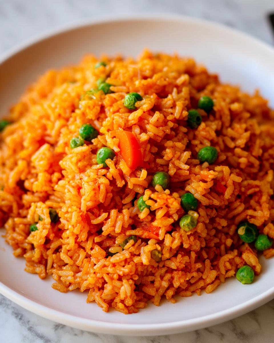 Close-up of bright orange Mexican rice mixed with green peas and diced carrots served on a white plate.