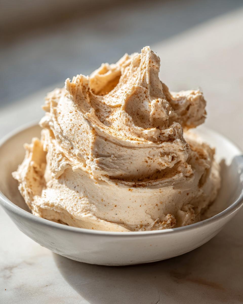 A close-up of fluffy, whipped cinnamon butter sprinkled with spice, served in a small white bowl.