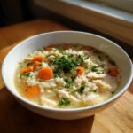 A close-up of a white bowl filled with homemade chicken and rice soup, garnished with fresh parsley.