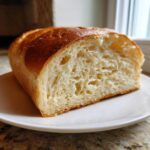 A close-up of a slice of soft, fluffy yeast bread showing the airy interior and golden-brown crust.