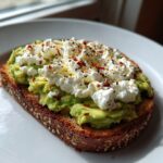 Close-up of avocado cottage cheese toast topped with pepper and chili flakes on a white plate.