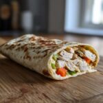 Close-up of a baked cottage cheese wrap filled with shredded chicken, diced carrots, and green peppers.