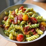 A close-up of a bowl filled with creamy, green-dressed blt pasta salad topped with crispy bacon pieces and halved cherry tomatoes.