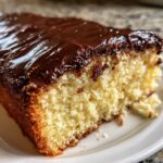 Close-up of a moist slice of boston cream pie poke cake topped with glossy chocolate ganache.