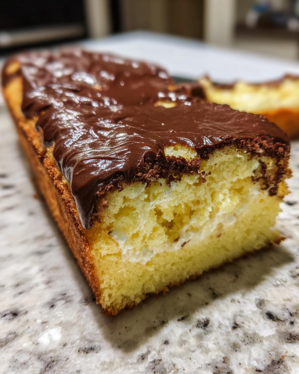 Close-up of a slice of boston cream pie poke cake showing the yellow cake, cream filling, and chocolate glaze.