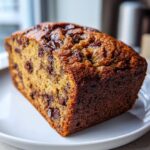 A freshly baked loaf of brown butter chocolate chip banana bread sitting on a white plate.