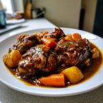 Close-up of tender brown stew chicken jamaican crock pot served with carrots and potatoes in a rich sauce.