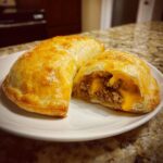Close-up of golden baked cheeseburger pockets biscuits, one cut open showing ground beef and melted cheese filling.