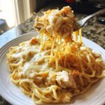 A fork lifting a cheesy, creamy portion of chicken spaghetti casserole, showing long cheese pulls.