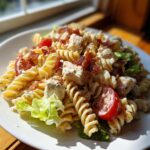 A close-up of creamy chicken BLT pasta salad featuring rotini pasta, chicken chunks, bacon bits, and cherry tomatoes.