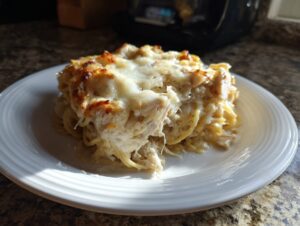A generous serving of creamy chicken spaghetti casserole topped with melted, browned cheese on a white plate.