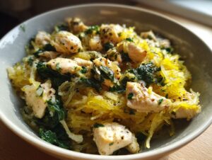 Close-up of a bowl filled with bright yellow chicken spaghetti squash mixed with wilted spinach and herbs.