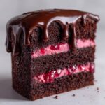 Close-up of a decadent slice of chocolate raspberry cake featuring dark layers, pink filling, and dripping chocolate ganache.